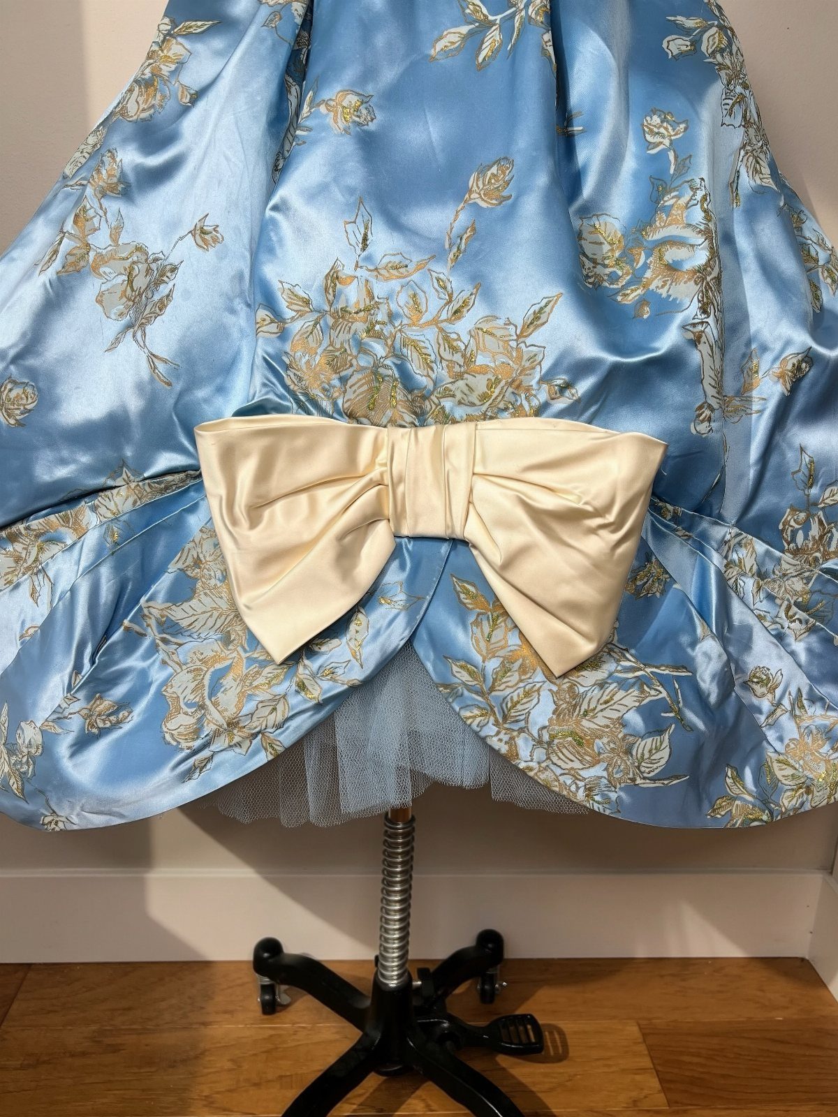Light blue satin dress with gold floral embroidery and a large cream bow.