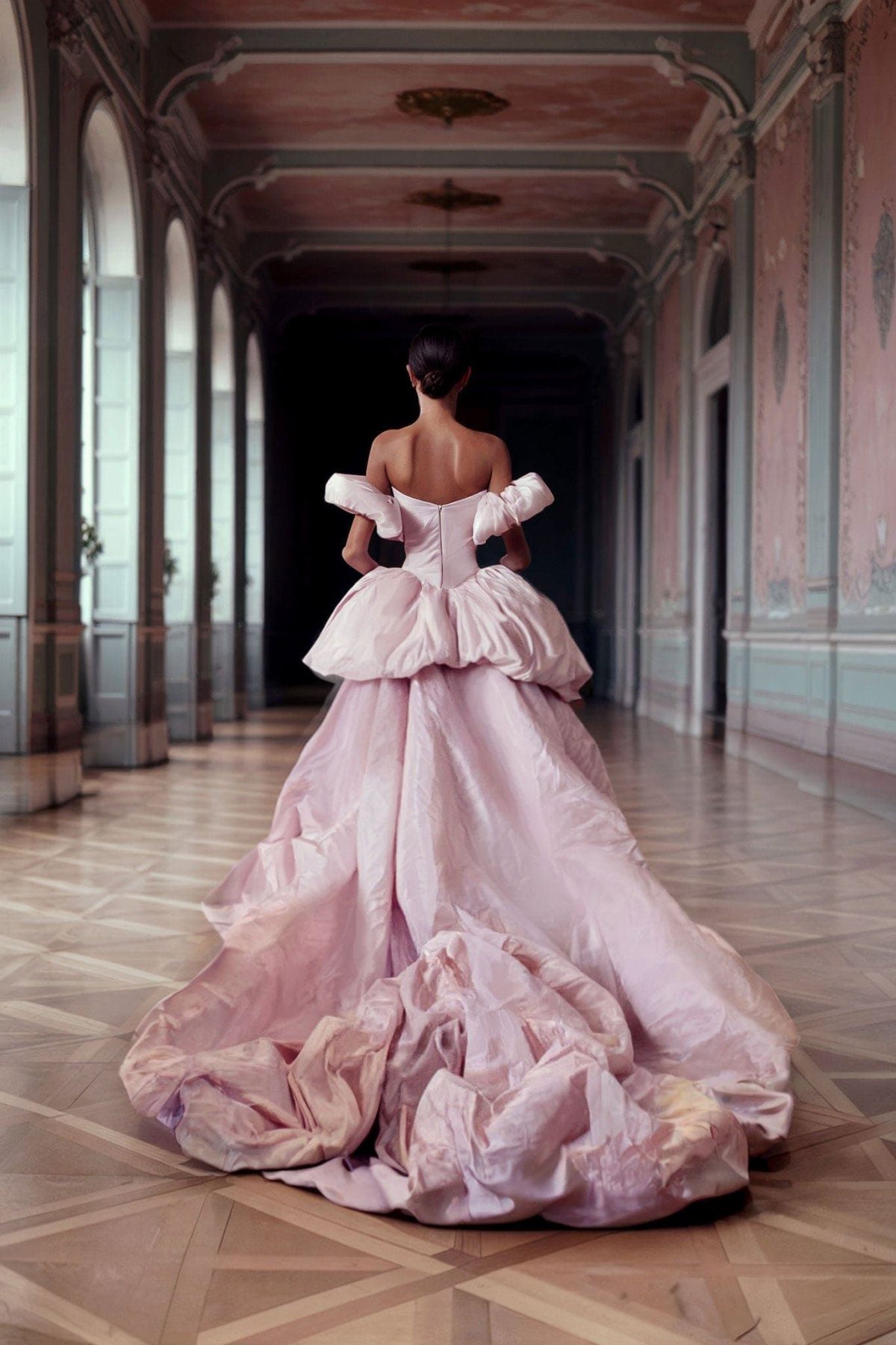 Woman from behind in a voluminous pink satin gown in an ornate hallway