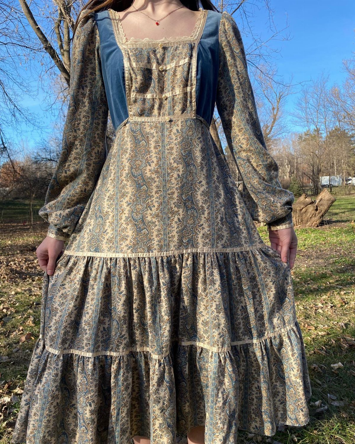 Tiered floral prairie dress with blue bodice and lace trim worn outdoors.