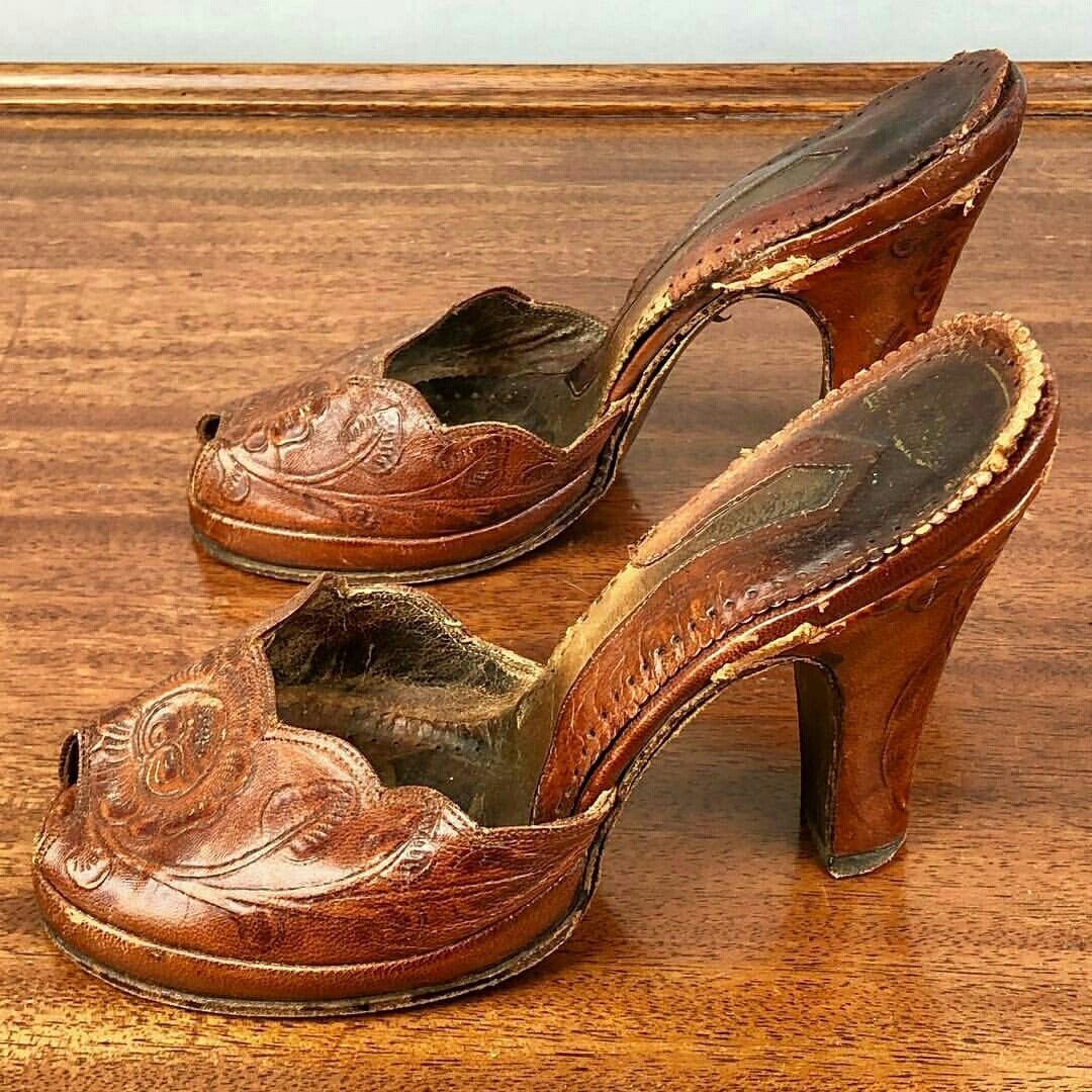 Brown leather vintage mule heels with embossed floral patterns on a wooden table