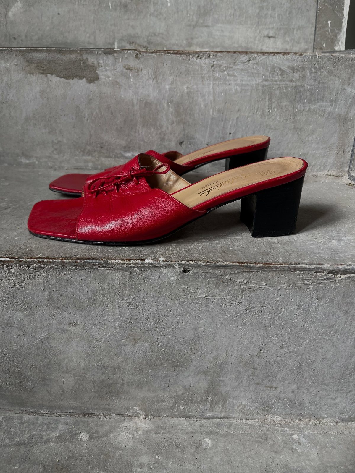 Red leather mule heels with square toes and black block heels on concrete steps
