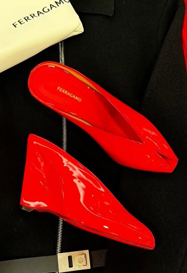Red patent leather pointed-toe mule heels resting on a black fabric background.