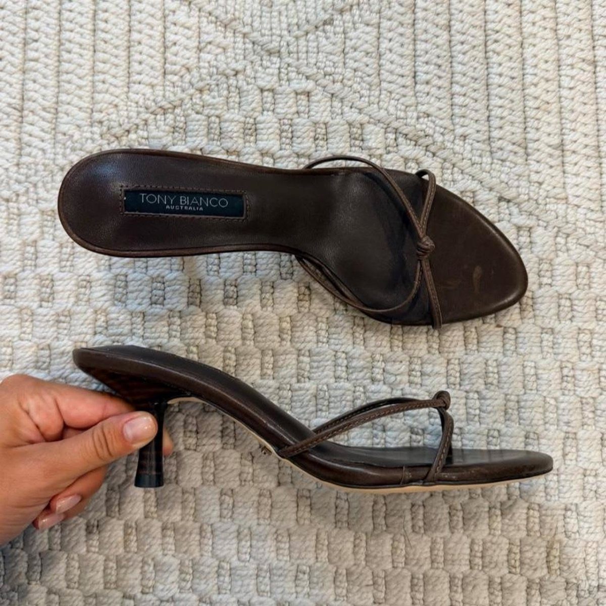 Dark brown leather Tony Bianco heeled mules with slim stiletto heels on white fabric.