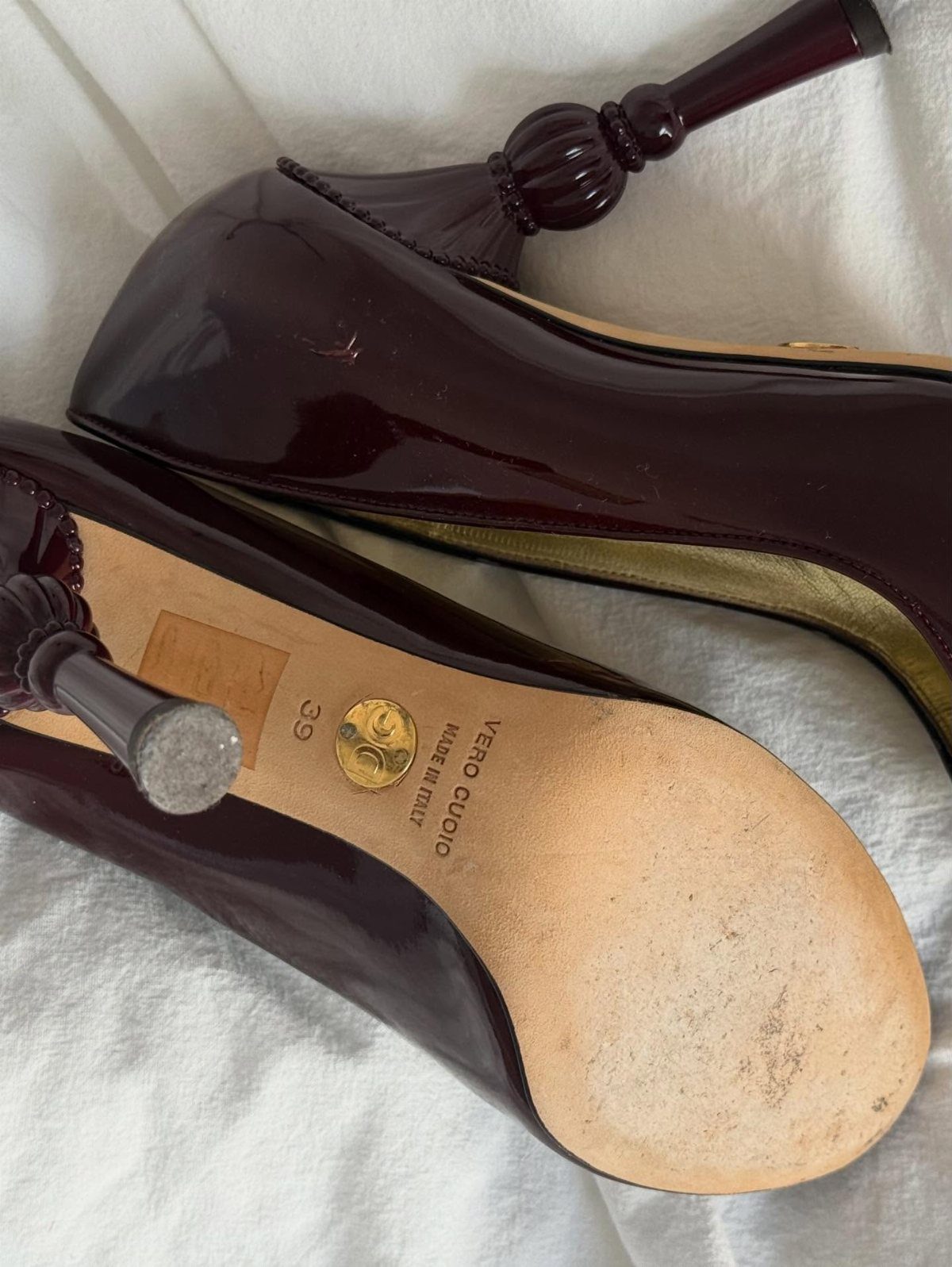 Burgundy patent leather high-heeled mules with carved heels on white fabric.