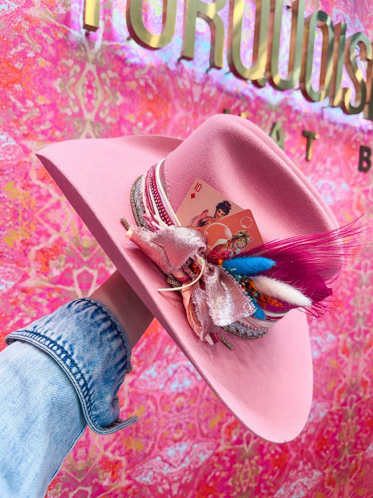 Western Themed Party Outfit Ideas: 8 Looks to Wear 1 Pink cowboy hat decorated with a sparkly bow and feathers held by a hand.
