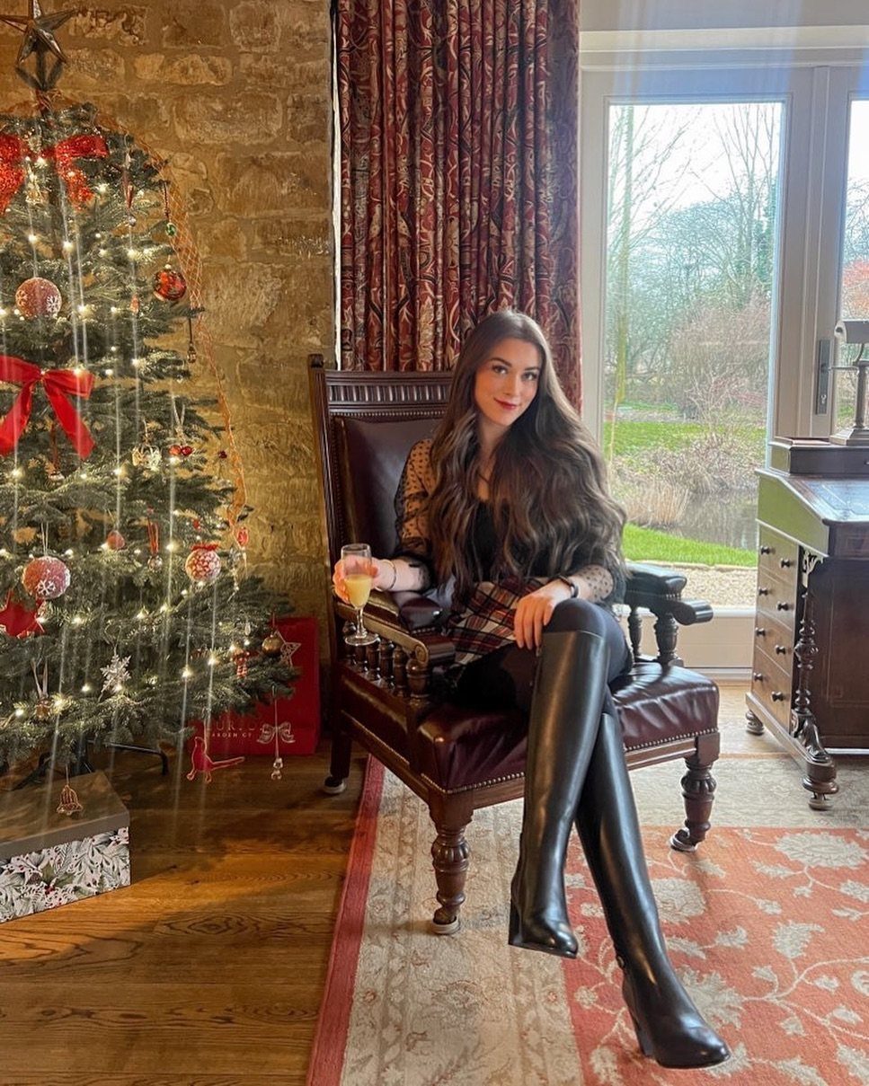 Woman in tartan mini dress and black over-the-knee boots sitting by Christmas tree