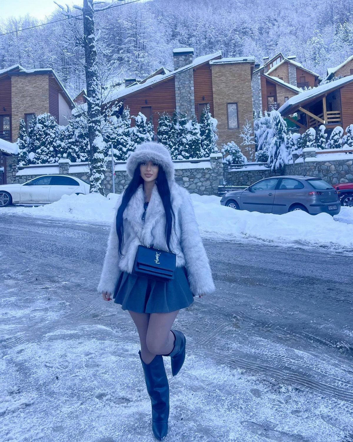 Woman in white faux-fur coat, short skirt, and tall black leather boots in snow