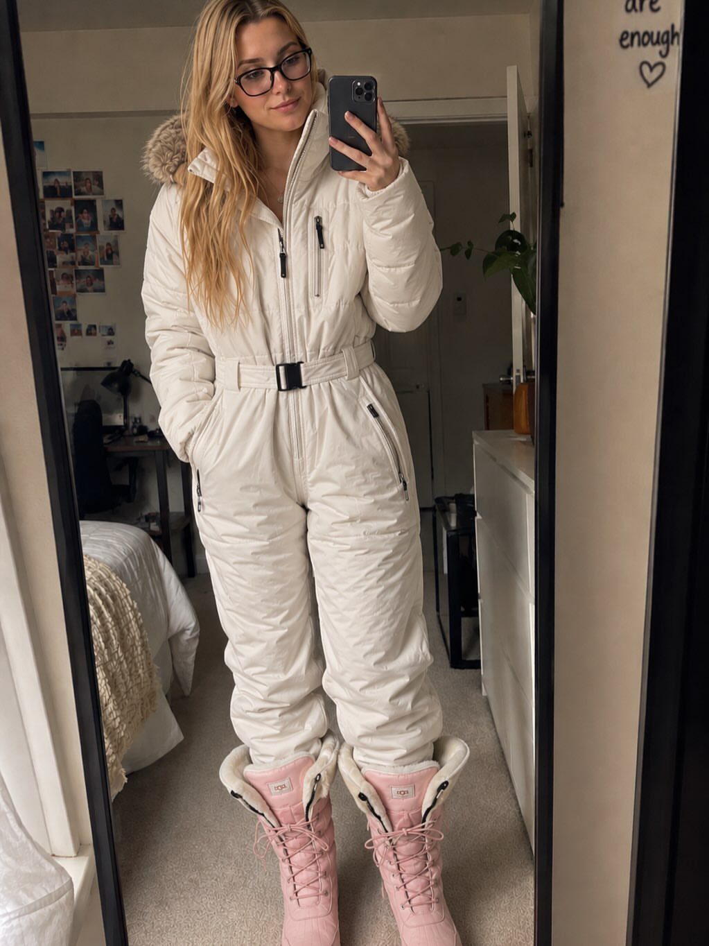 Woman in white quilted winter jumpsuit and pink lace-up snow boots taking selfie