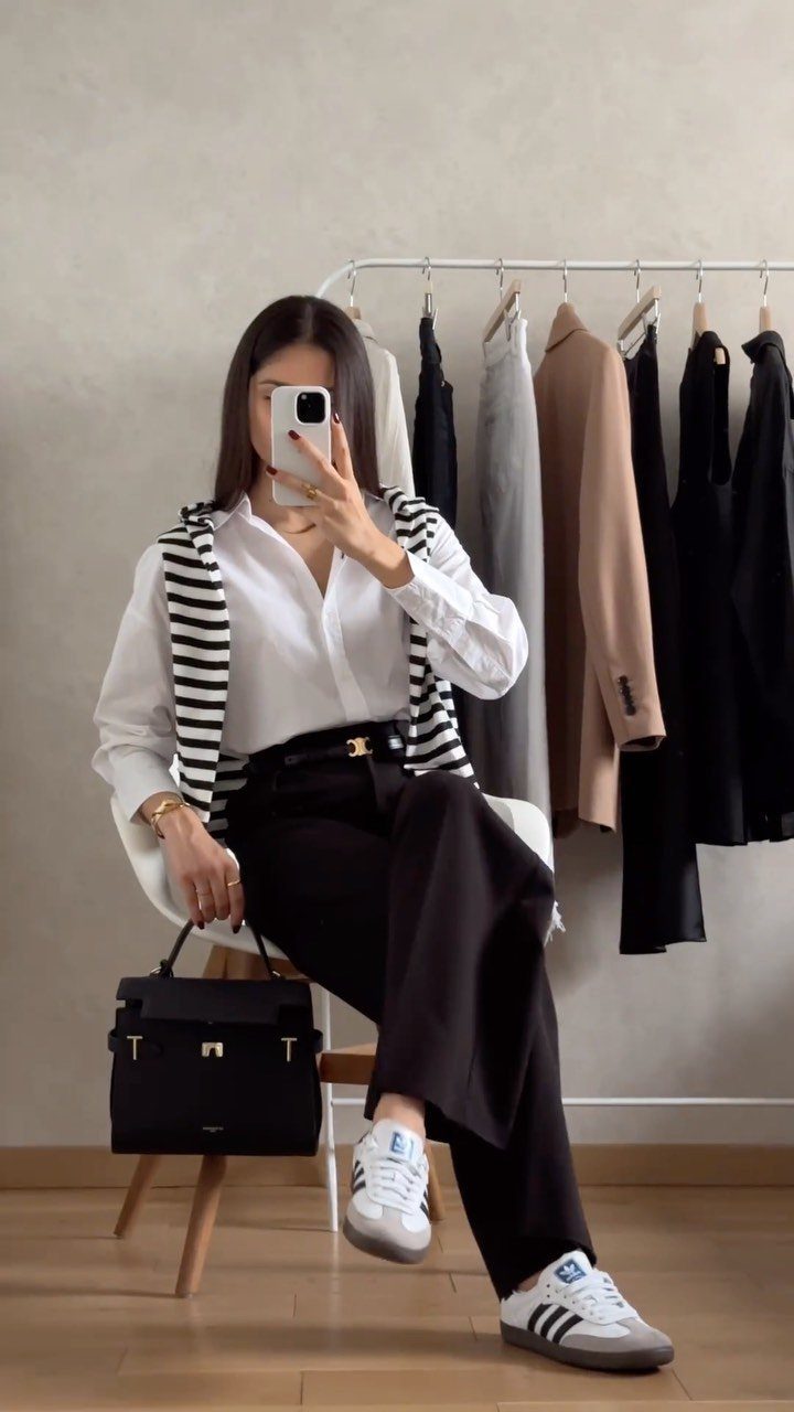 Woman wearing wide-leg black pants, white shirt, and sneakers posing for a selfie.