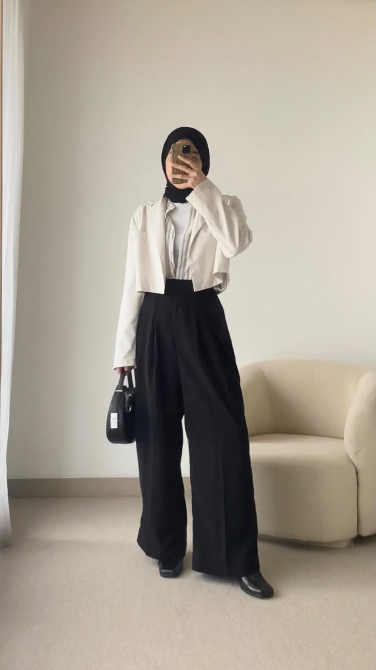 Person in a white cropped blazer and wide-leg black trousers posing for a selfie.